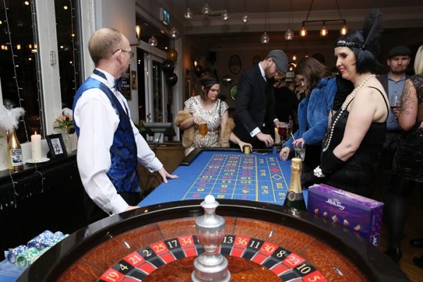 Croupier spinning the roulette wheel for guests at a 1920s themed party