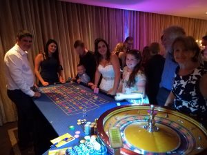 Wedding guests gathered around a roulette table in a softly lit room