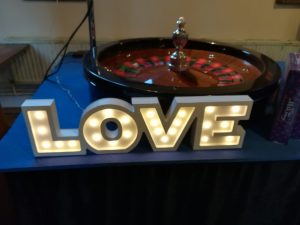 Roulette wheel behind a light-up LOVE sign at a wedding