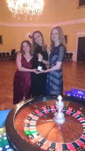 Three guests in evening dresses behind the roulette wheel