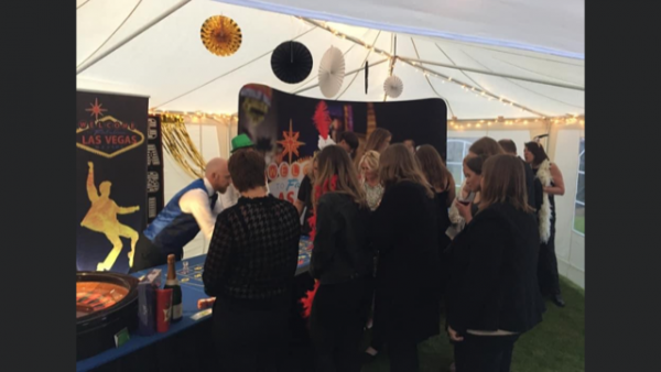 Guests crowded around casino tables at a Las Vegas themed marquee party
