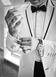 Man in a white dinner jacket and bow tie adjusting his cufflinks, black and white photo