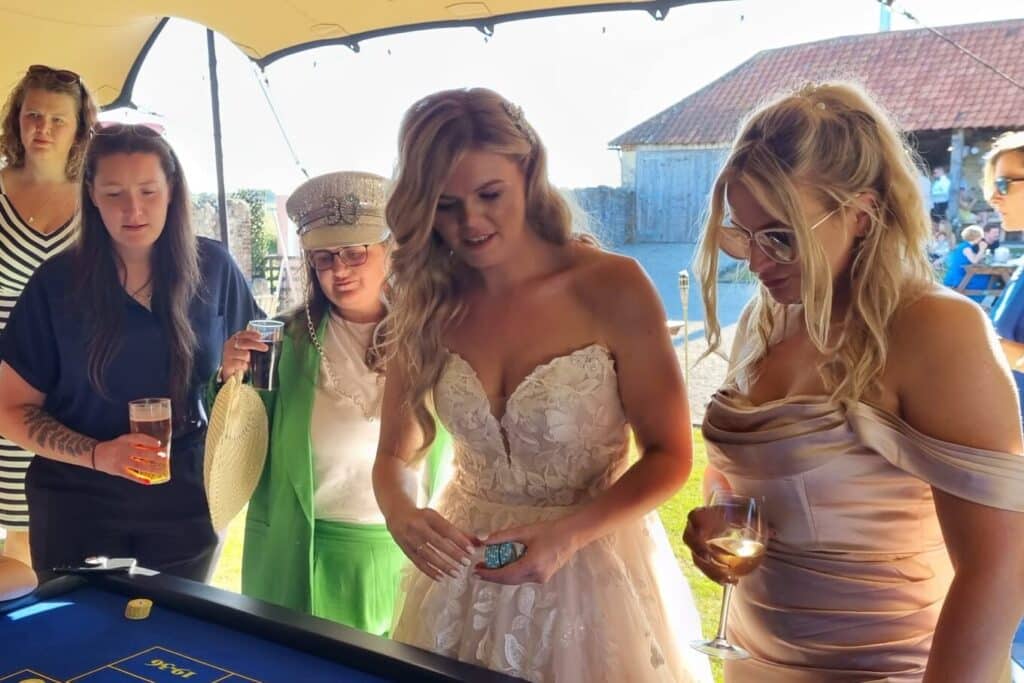 Bride placing chips on a fun casino roulette table with guests at an outdoor summer wedding reception