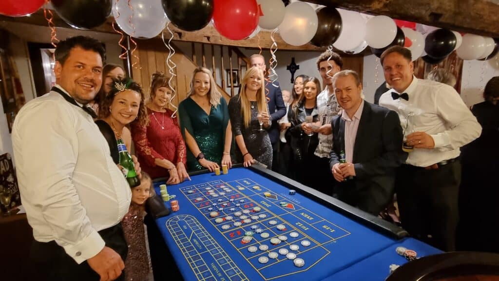 Black tie guests and croupier at a roulette table with balloons