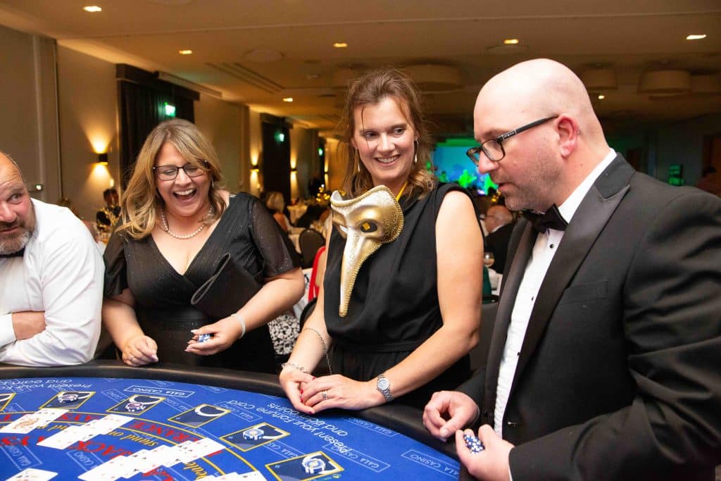 Guests in evening wear and a masquerade mask at a blackjack table