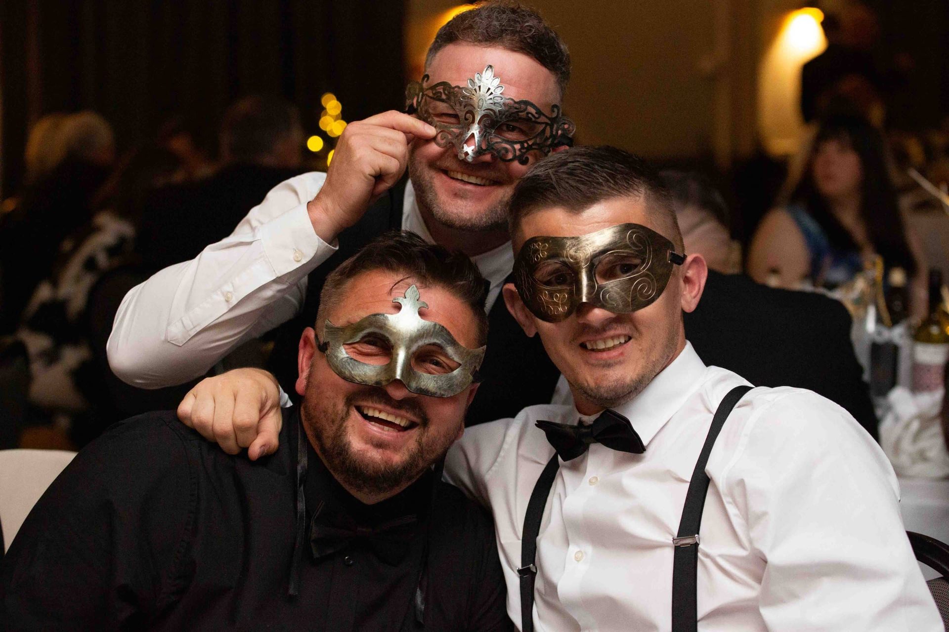 Three guests in masquerade masks at a black tie event